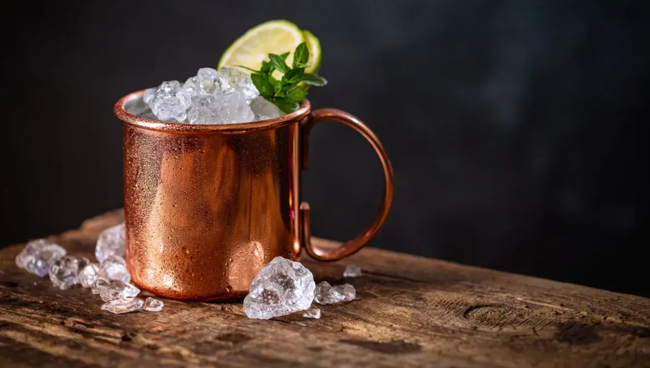 En kopp moscow mule fylld med is, garnerad med lime och mynta, st&aring;r p&aring; ett tr&auml;bord.