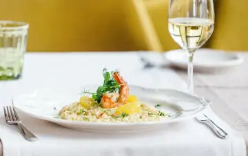 En elegant tallrik med saffransrisotto, toppad med en saftig räka och citrusklyftor. Ett glas vitt vin till saffransrisotto fulländar denna läckra måltid.