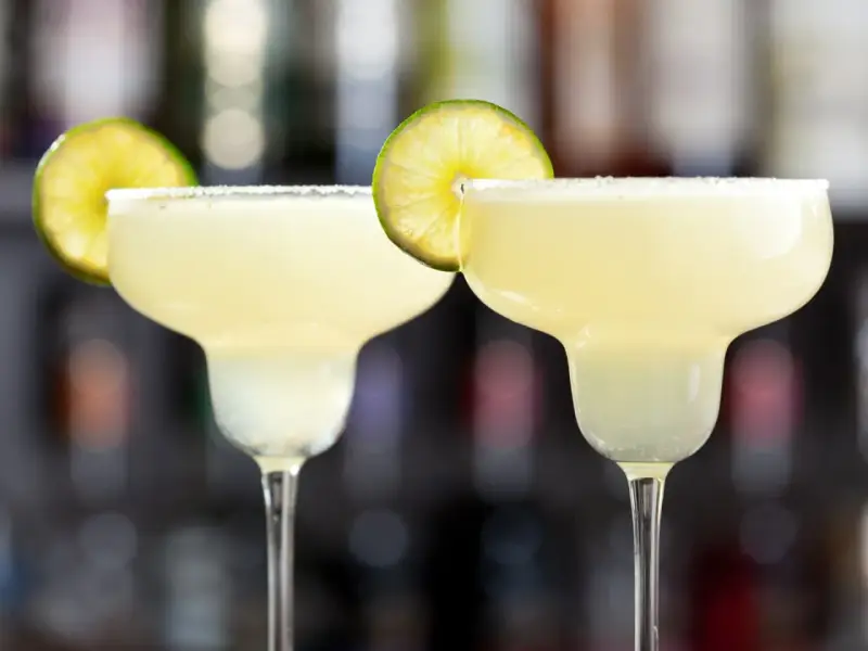 Två frostiga frozen margaritas med saltkant och lime, redo att avnjutas.