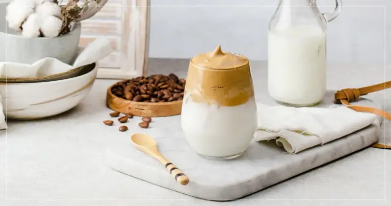 En krämig dalgona coffee med fluffigt skum, serverad med mjölk och kaffebönor.