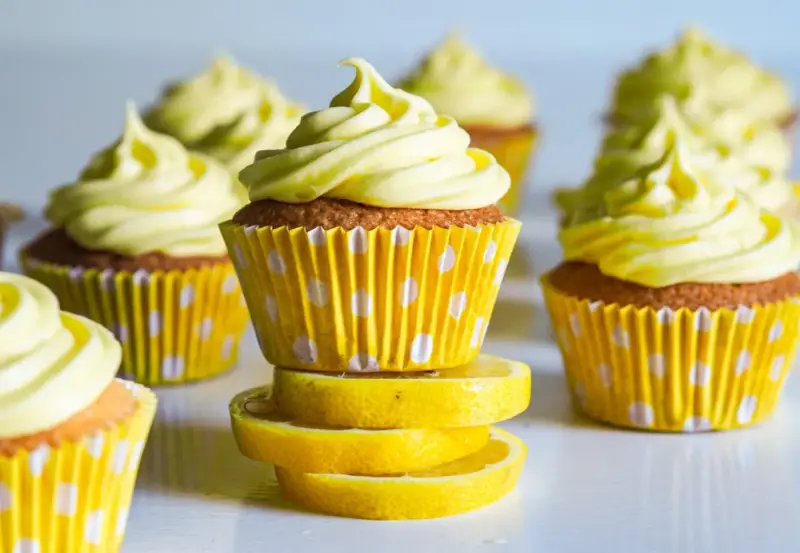 Gula citronmuffins med fluffig frosting, serverade i prickiga formar. Perfekt för ett citronmuffins recept!