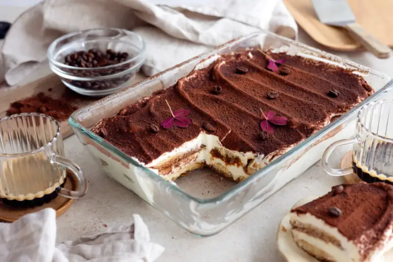 En krämig tiramisu i glasform, perfekt för ett enkelt tiramisu recept. Toppad med kakao, kaffebönor och lila blommor.
