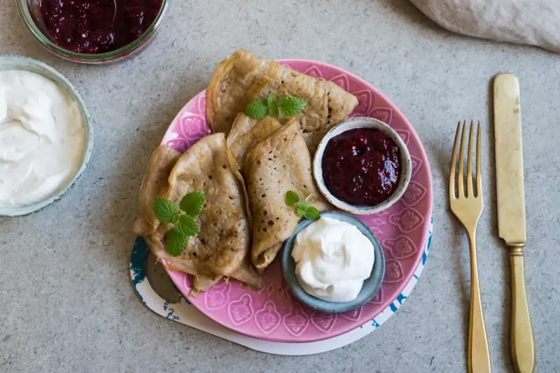 En tallrik med glutenfria pannkakor, serverade med sylt och grädde. En härlig frukost eller fika!