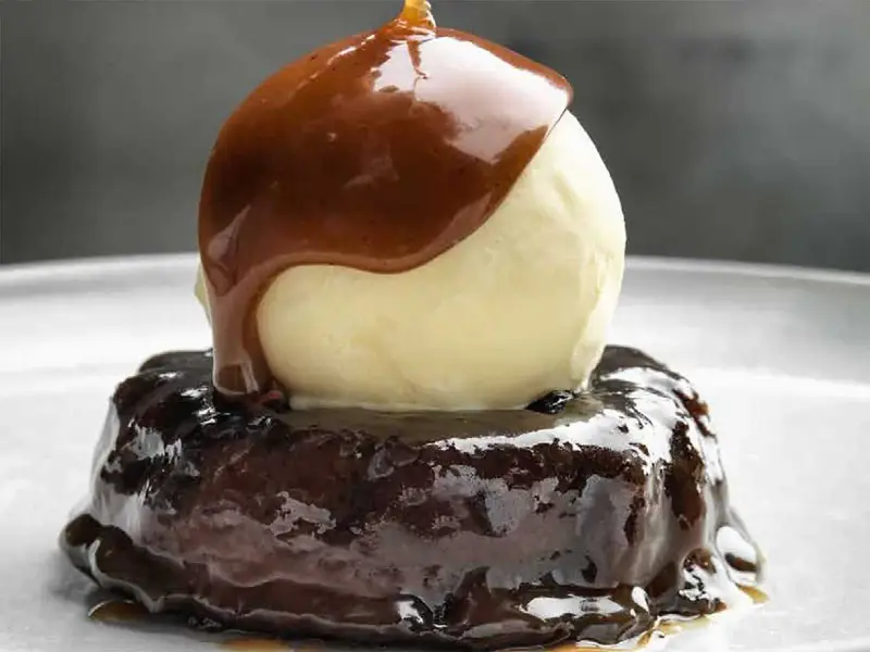 En läcker sticky toffee pudding med en kula vaniljglass och varm kolasås som rinner över.